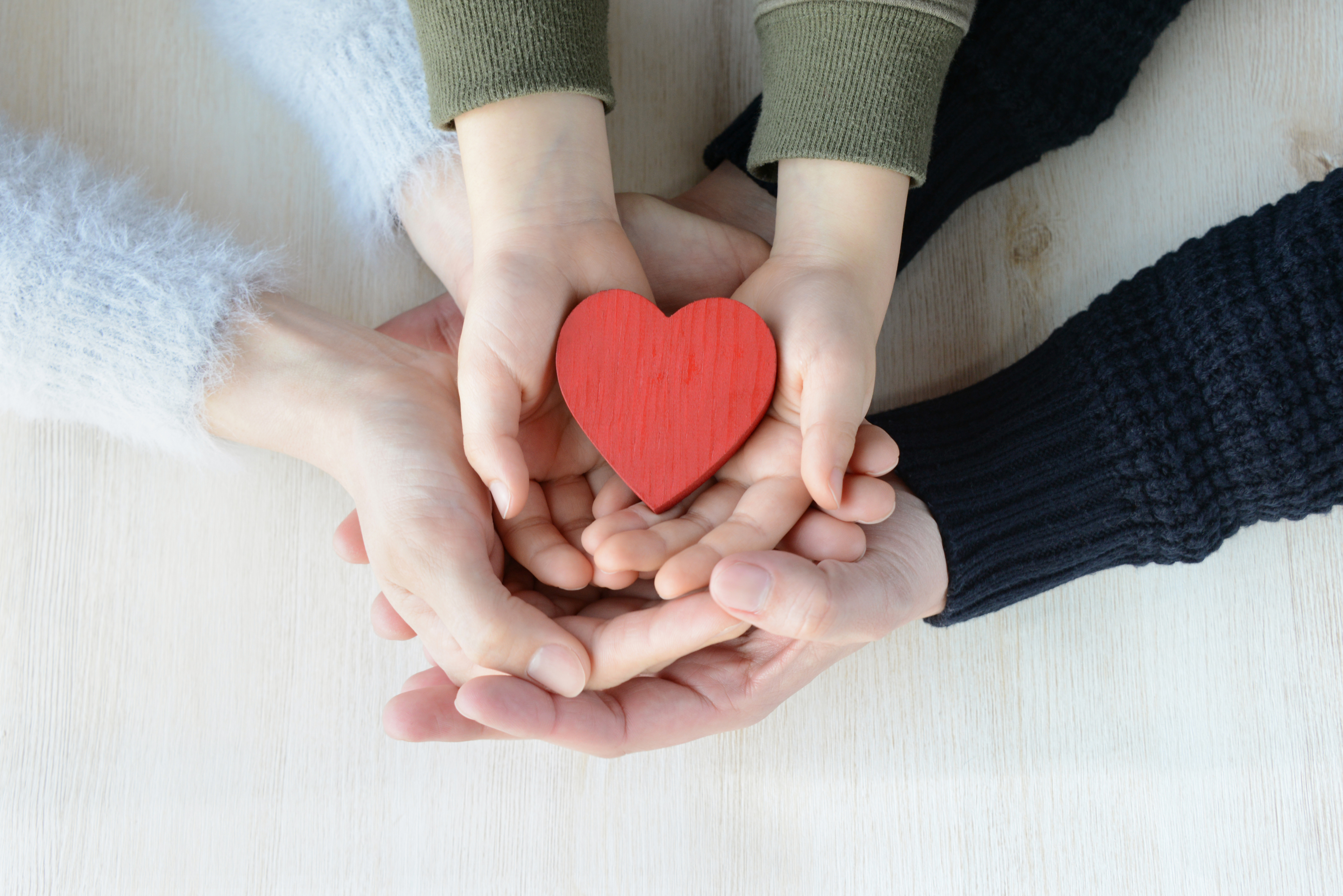 two sets of adults hands and one child hands stacked with palms facing upwards and holding a toy heart